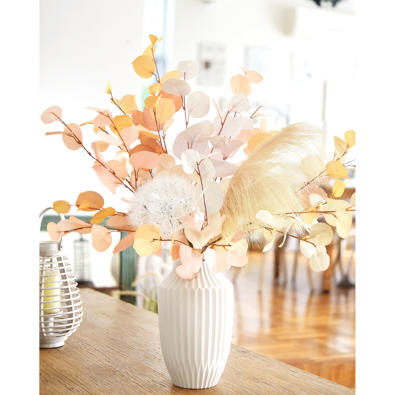 A stunning autumn-themed arrangement with dusky pink, beige, and soft yellow eucalyptus stems and pampas grass in a white vase, displayed on a light wooden table. This decor is ideal for creating a warm and cozy atmosphere in any living space.