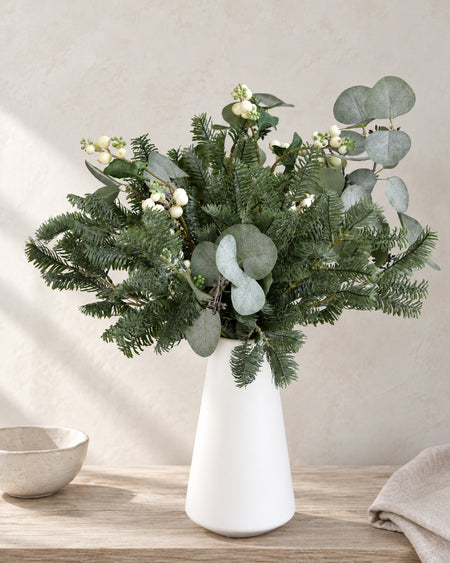 Artificial pine stems arranged in a white vase for winter home decor
