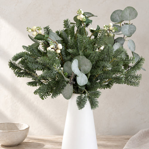 Artificial pine stems arranged in a white vase for winter home decor