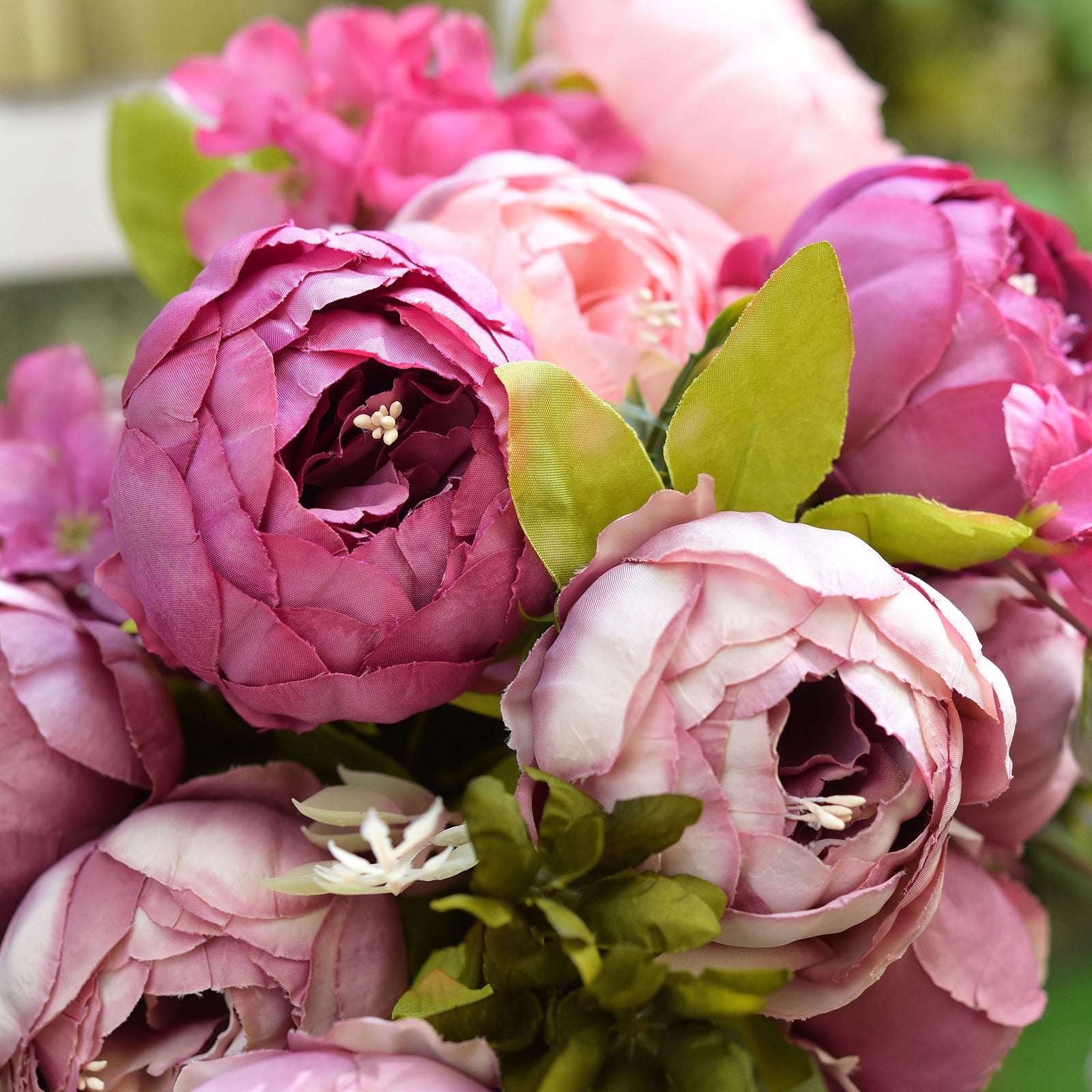 A mixed artificial peony arrangement in a rustic green vase, placed in an outdoor setting for a natural, vibrant look.