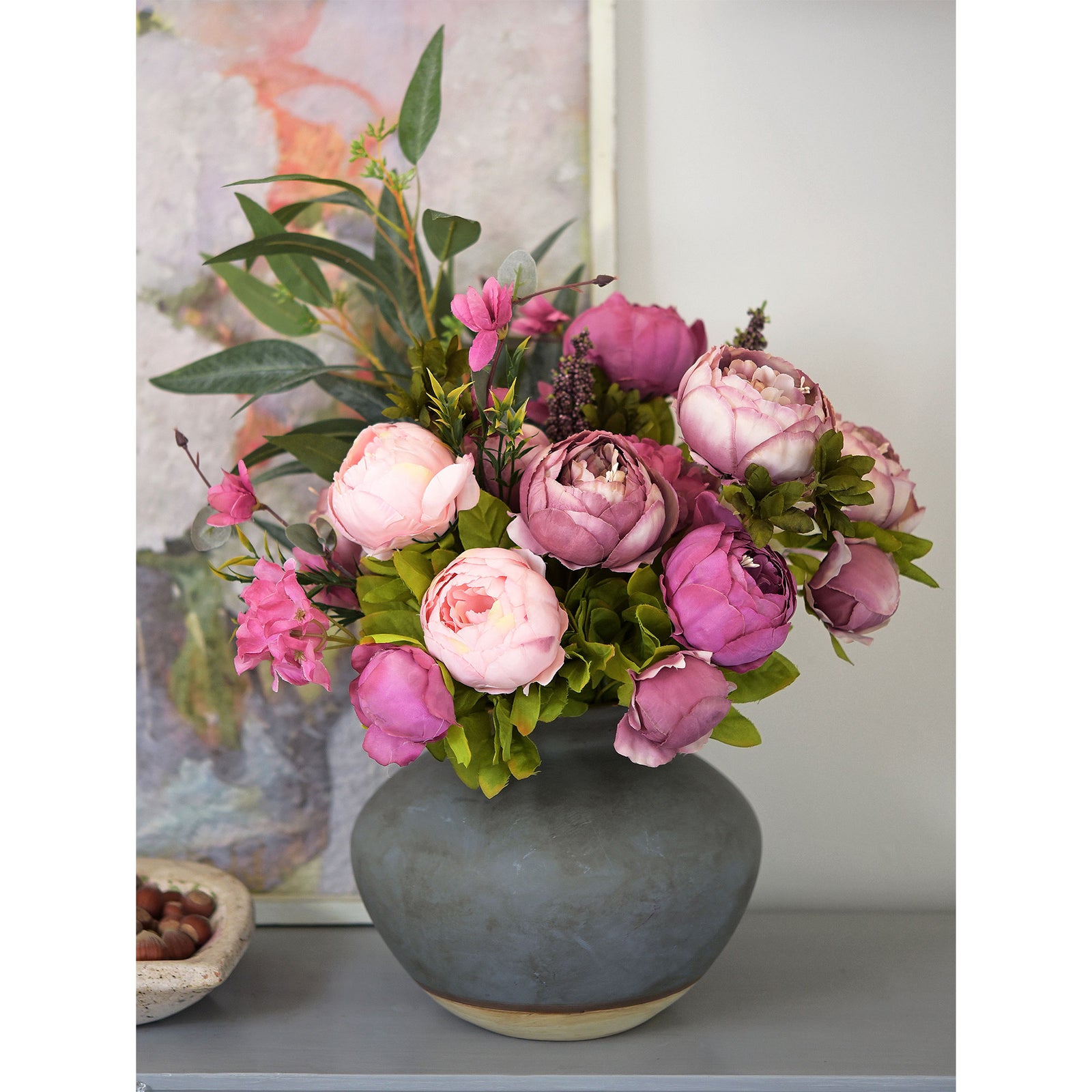 A soft and elegant peony and hydrangea arrangement in shades of pink and purple, displayed in a grey ceramic vase.