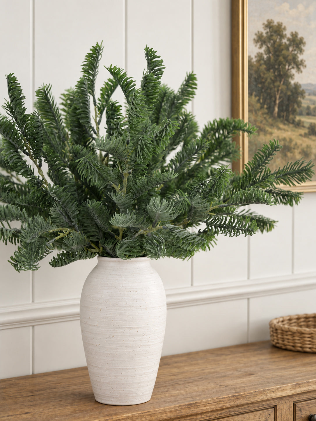 Artificial pine stems arranged in a white pitcher on a farmhouse console