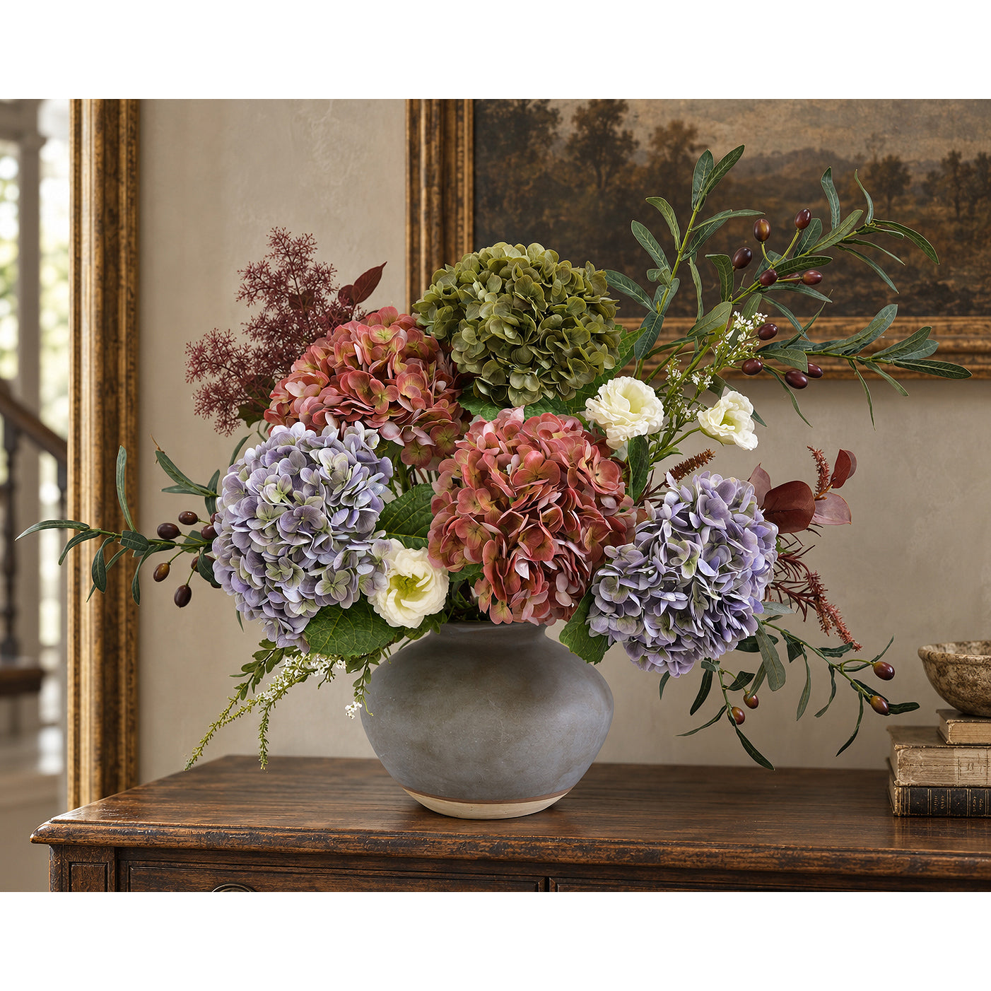 Antique lavender hydrangeas with brick rose and olive flowers in a gray bowl-shaped vase on a foyer console.