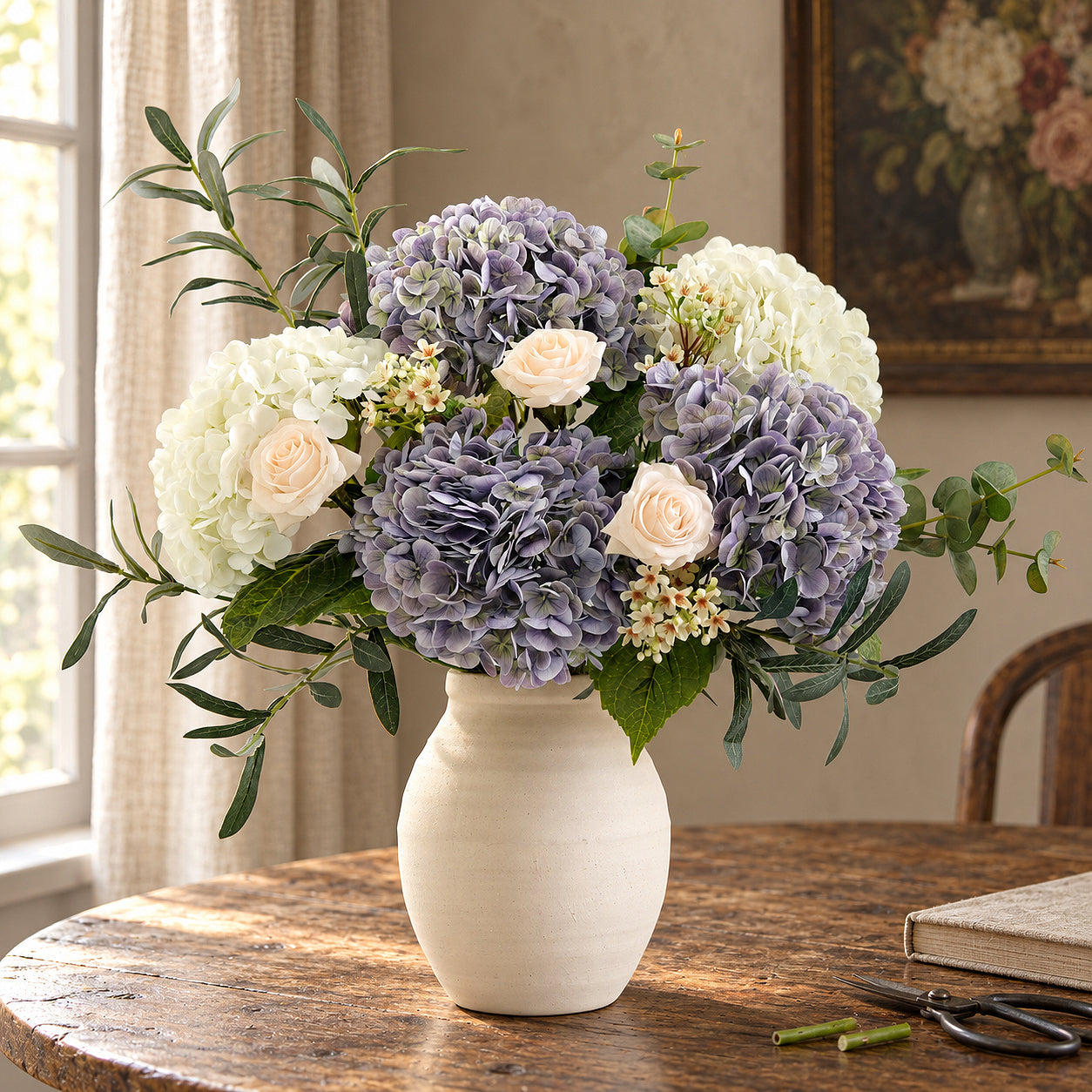 Three antique lavender hydrangeas with white flowers, pale roses and greenery in a cream vase.