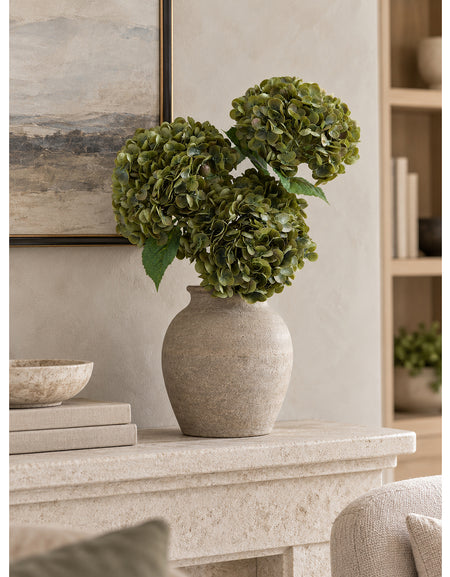 Three antique olive hydrangeas in a gray vase on a limestone mantel.