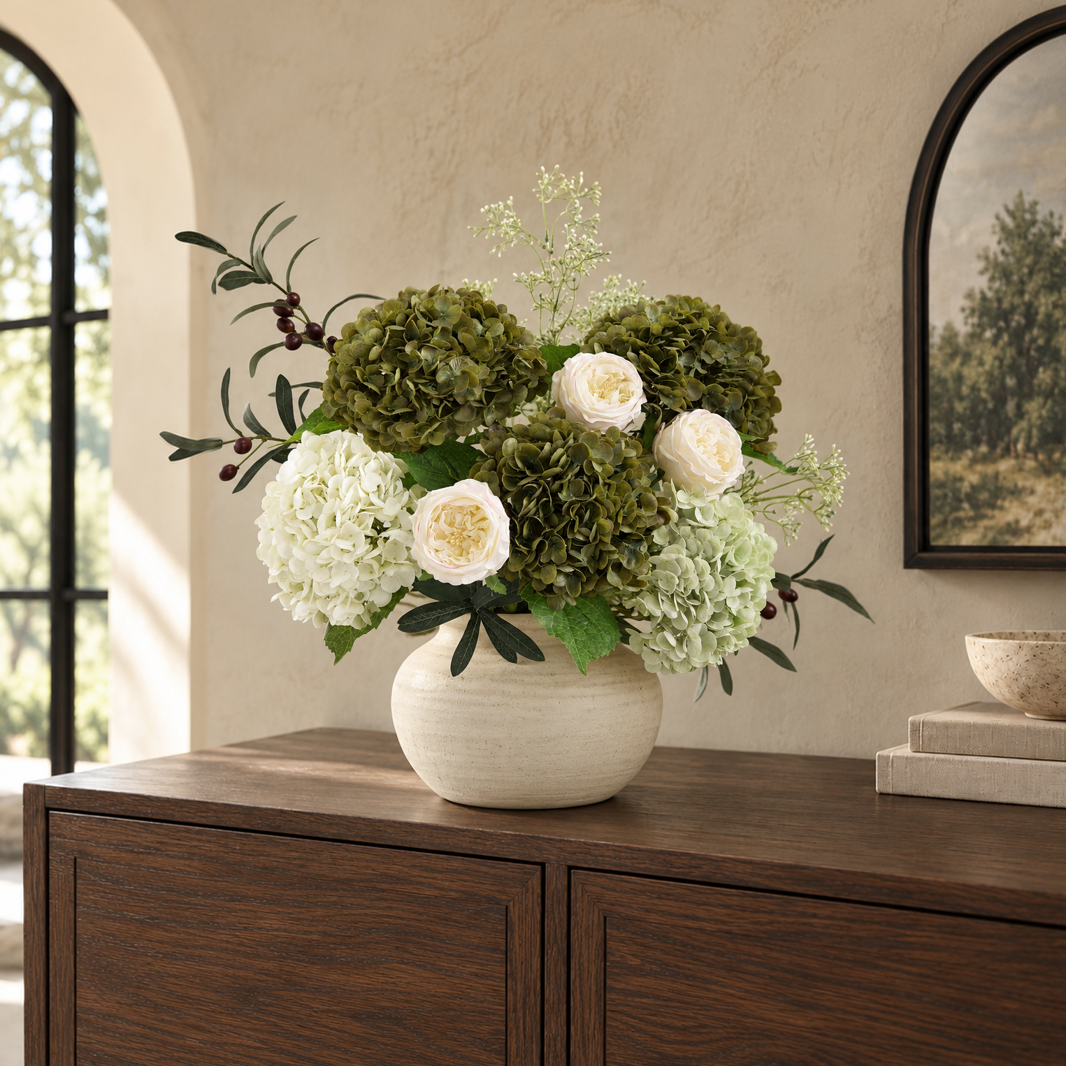Antique olive hydrangeas with white flowers, cream roses and greenery in a pale vase on a sideboard.
