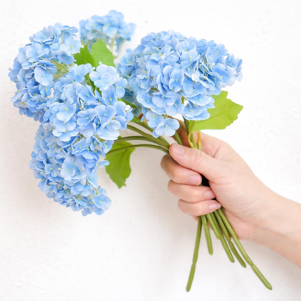 Hand holding six blue real touch hydrangea stems to show bouquet size and scale.