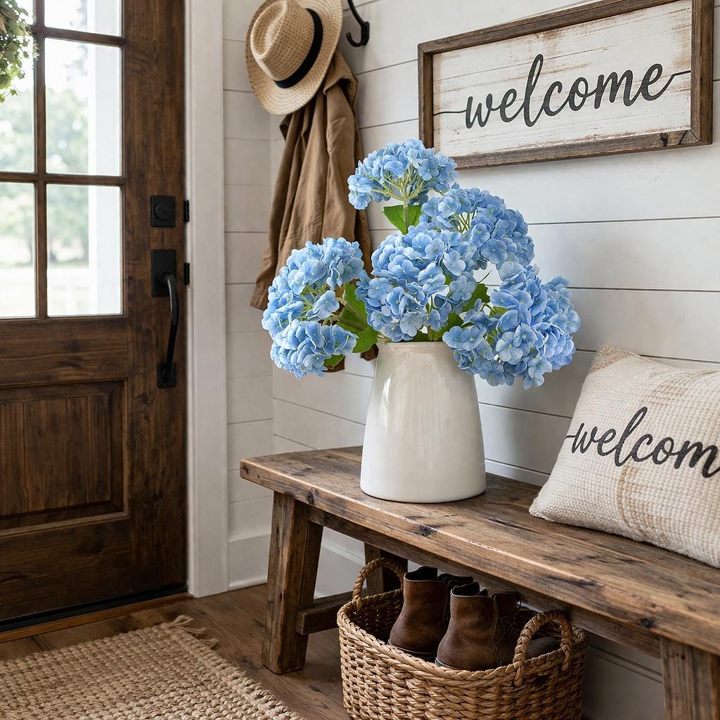 Blue real touch hydrangea stems arranged in a white pitcher vase on a farmhouse entryway bench.