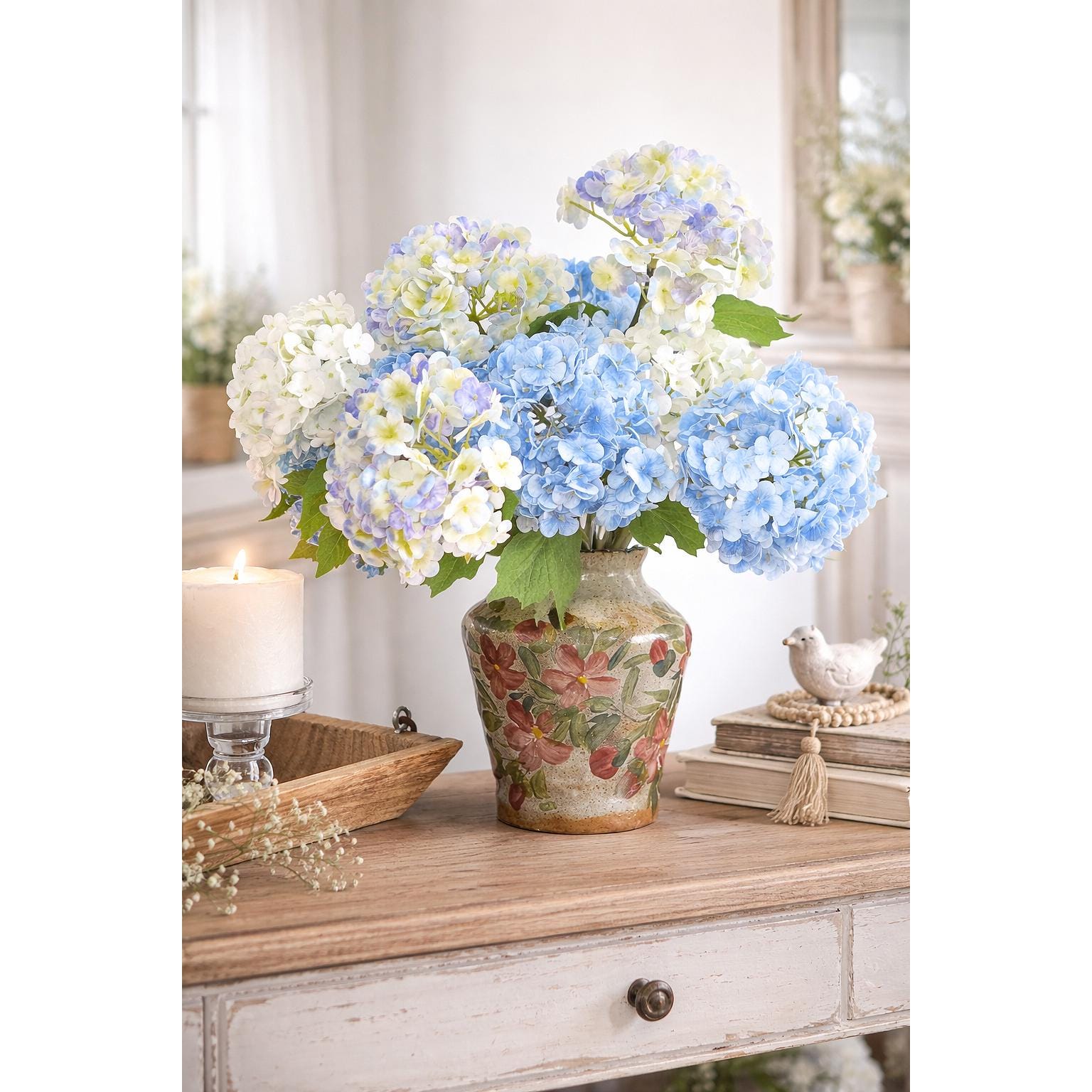 Blue and white real touch hydrangea stems arranged in a vase on a wooden dresser.
