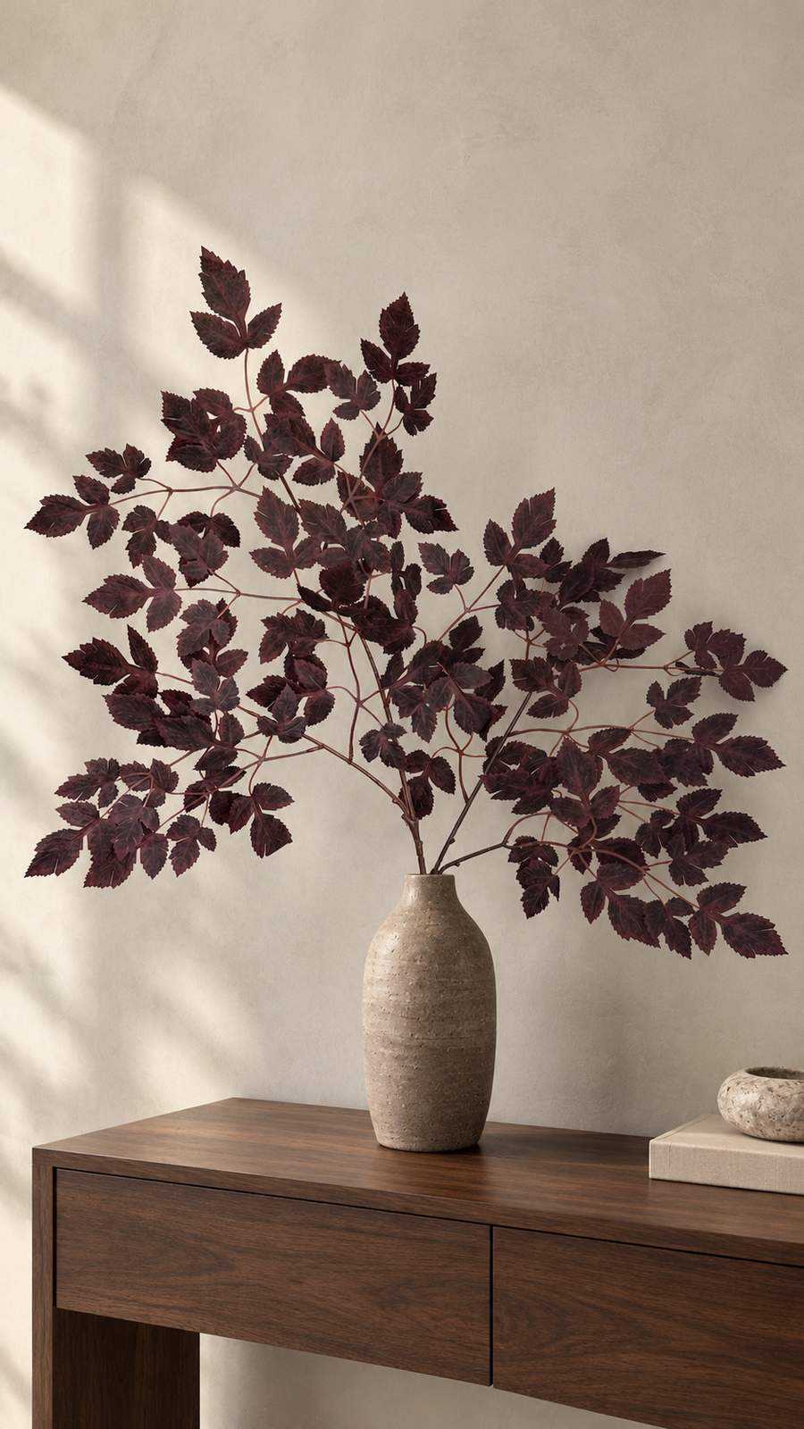 Burgundy maple foliage spreading from a beige vase on a wooden console.