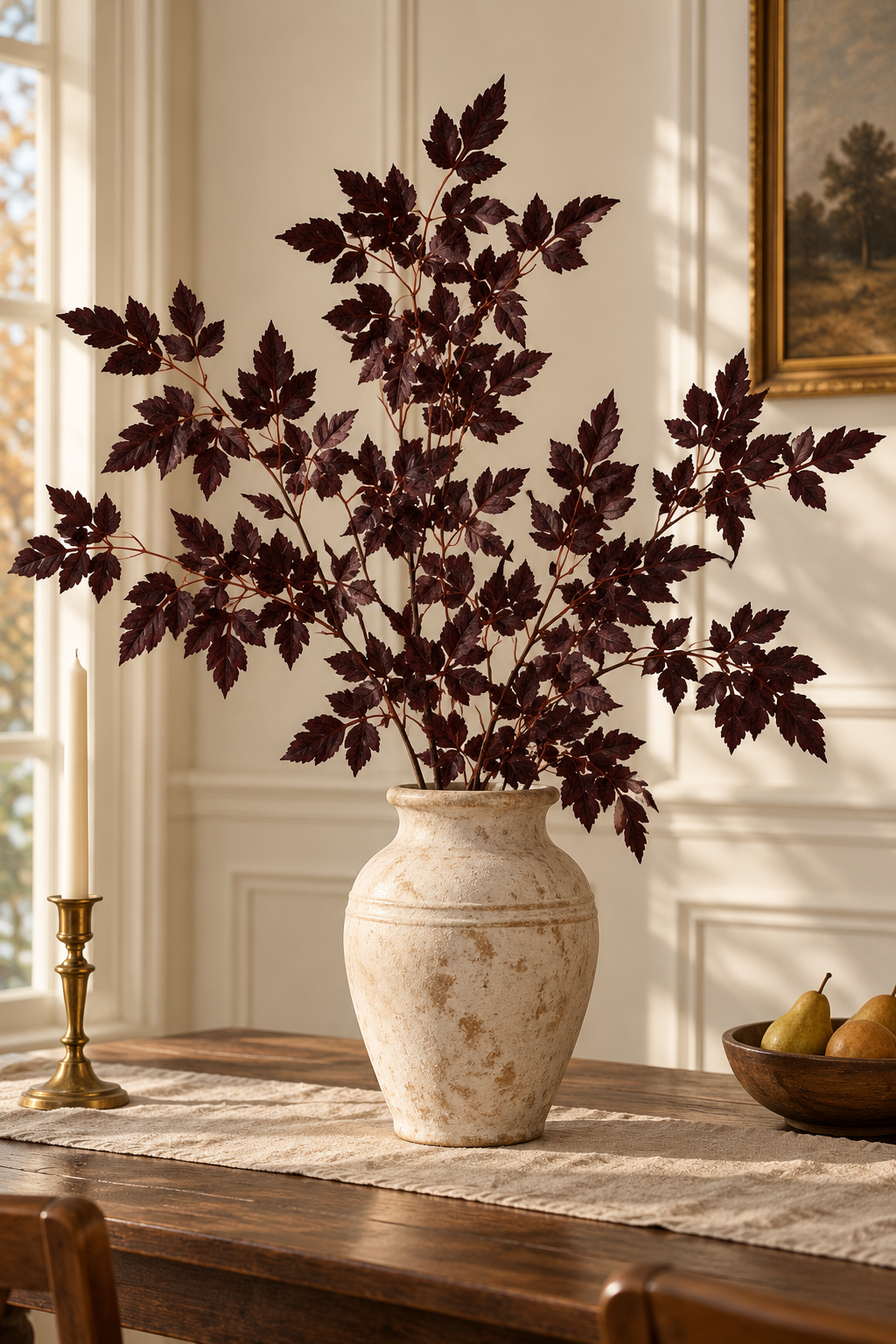 Full burgundy foliage arrangement in an ivory urn beside a candle on a wooden table.