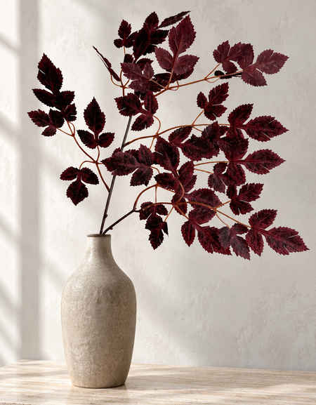 Burgundy maple foliage in a narrow beige vase on a sunlit stone surface.
