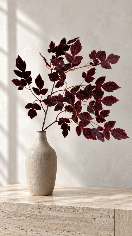Burgundy maple foliage in a narrow beige vase on a sunlit stone surface.