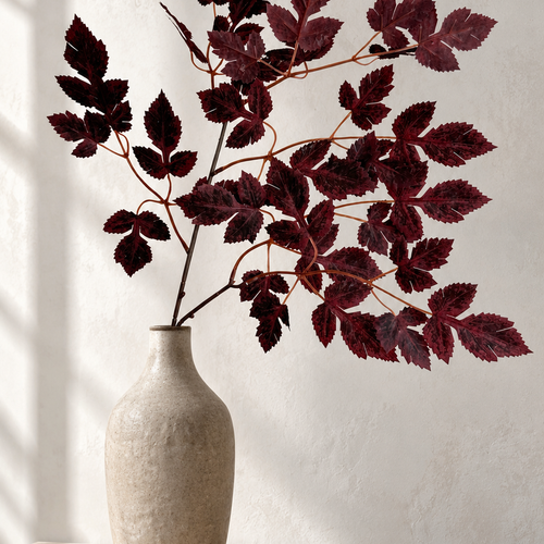 Burgundy maple foliage in a narrow beige vase on a sunlit stone surface.