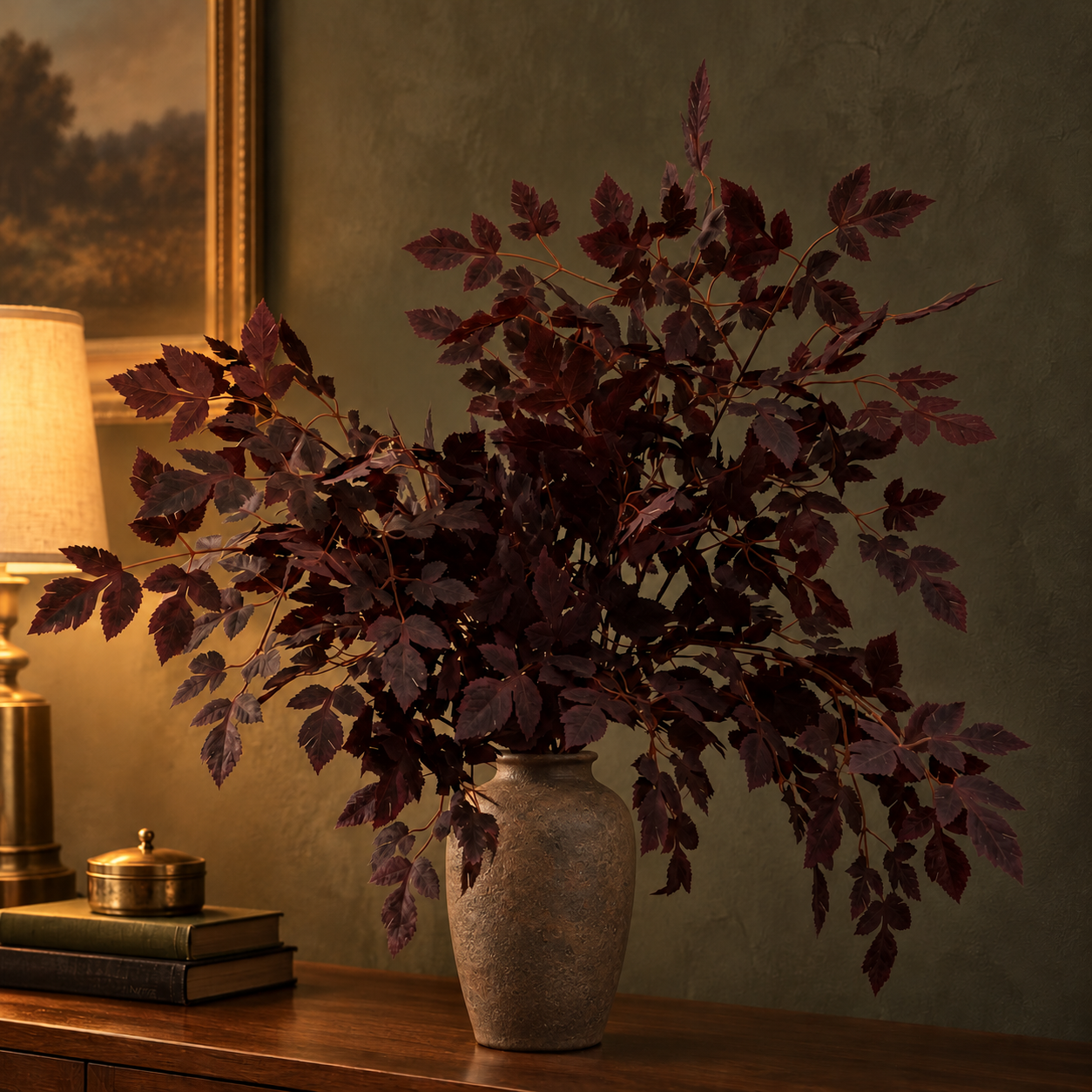Burgundy foliage in a taupe vase beside a table lamp in a warm interior.