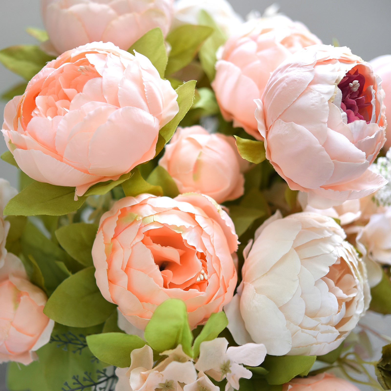 Close-up view of peach and blush artificial peonies, showing detailed silk petals and soft green leaves for lifelike realism.