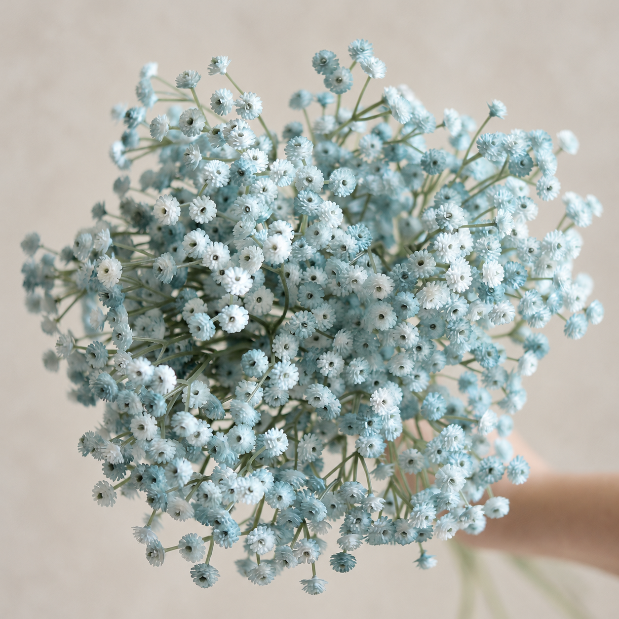 Rounded cluster of pale blue artificial baby's breath flowers with branching green stems against a warm neutral background.