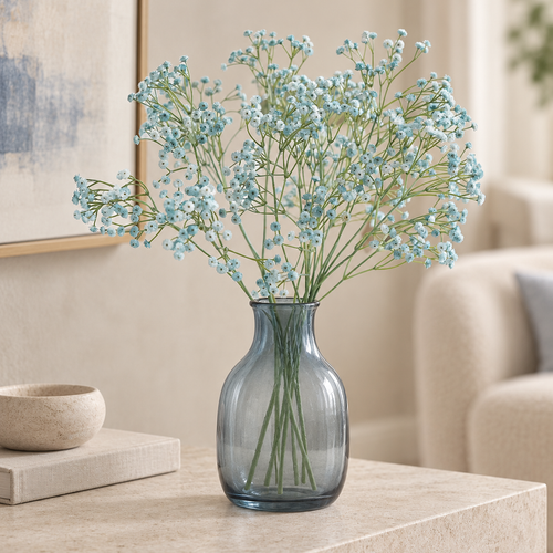 Airy dusty blue artificial baby's breath stems arranged in a smoky blue glass vase on a stone table.