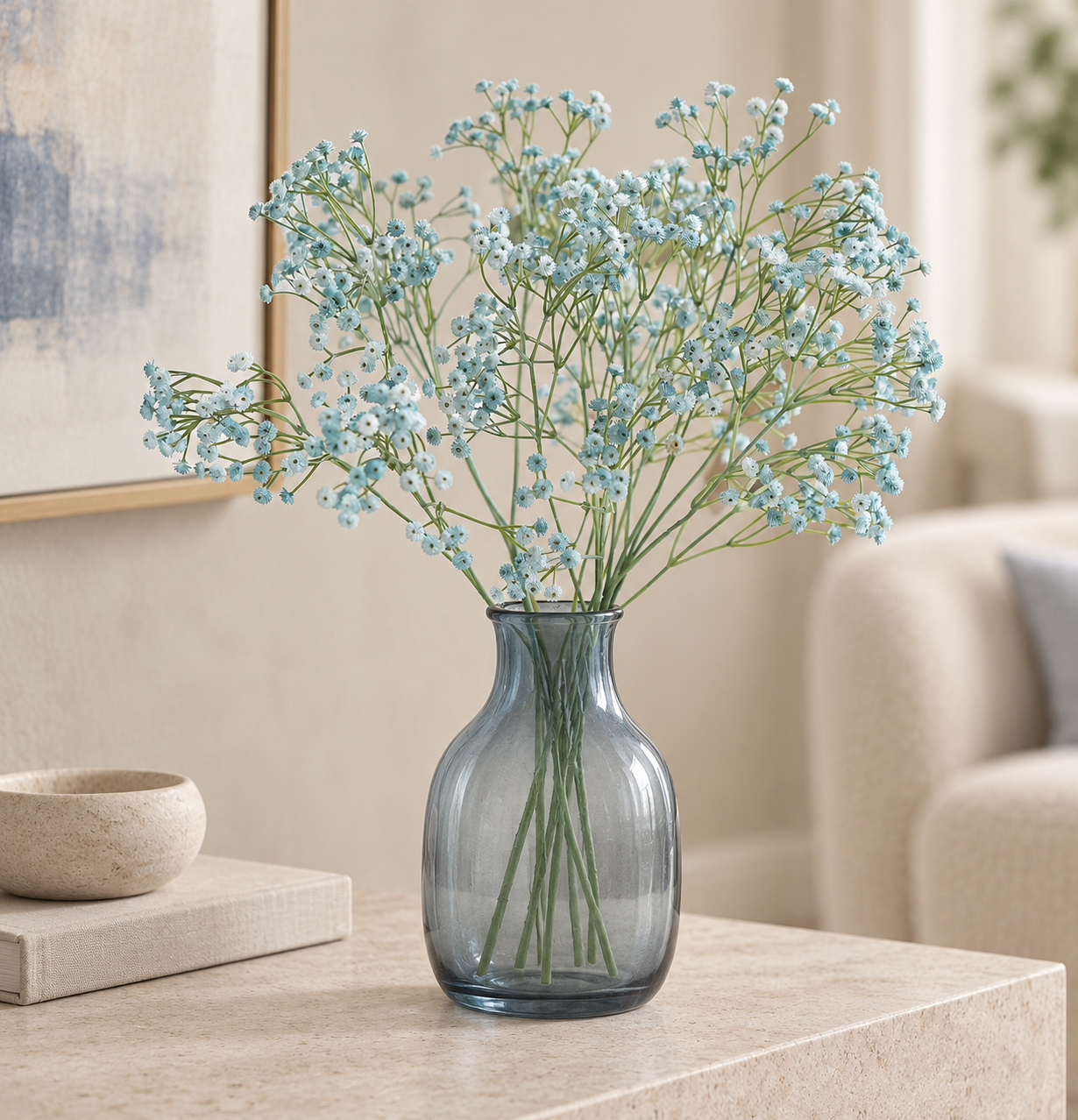 Airy dusty blue artificial baby's breath stems arranged in a smoky blue glass vase on a stone table.