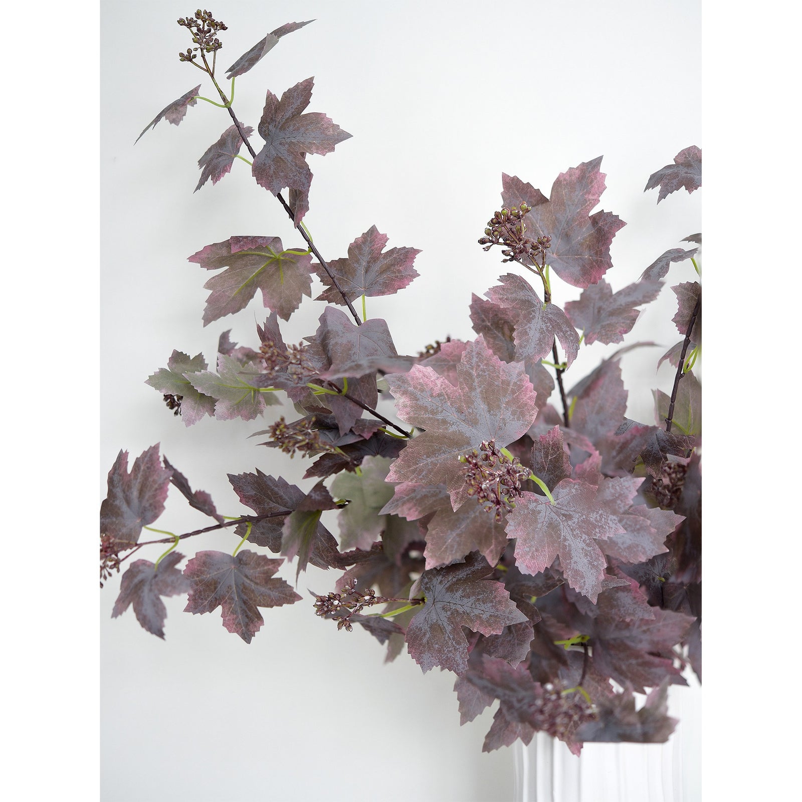 Dusty mauve brown artificial maple foliage arranged in a white ribbed vase, with branching stems and mottled leaves.