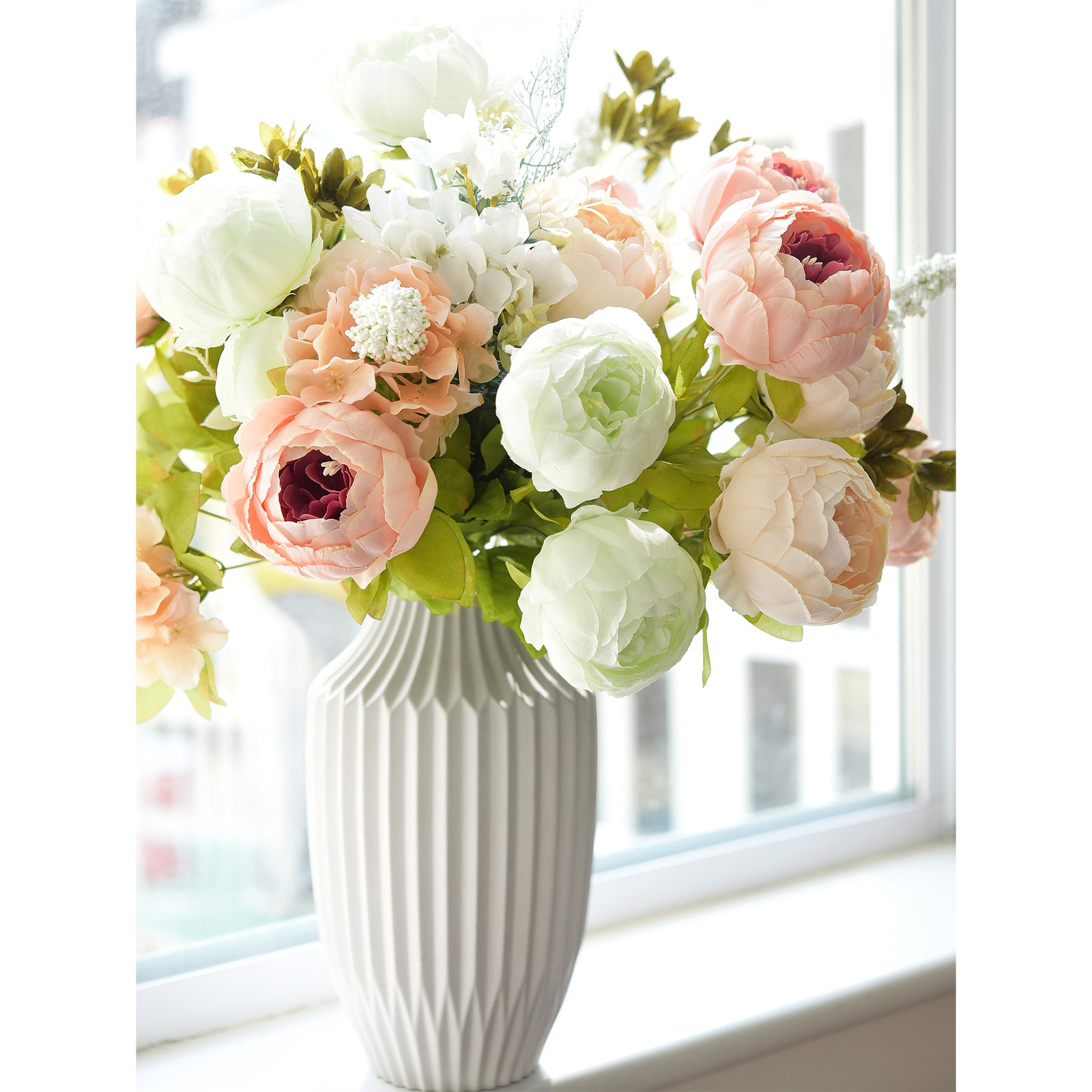 Green and blush floral arrangement featuring peonies and greenery in a ribbed ceramic vase, ideal for window décor.