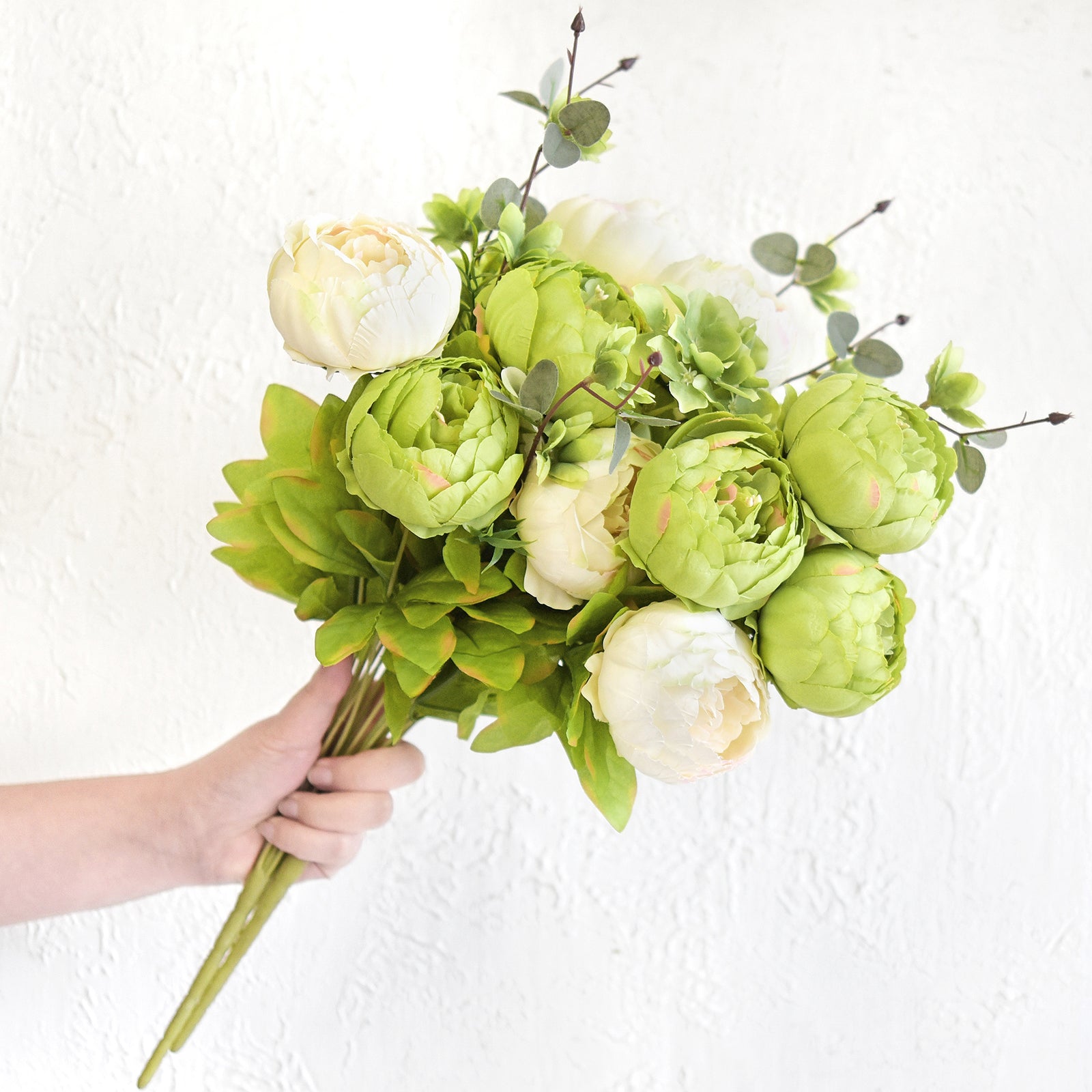 Hand holding moss green and cream artificial peony bouquet bundles to show size and fullness.