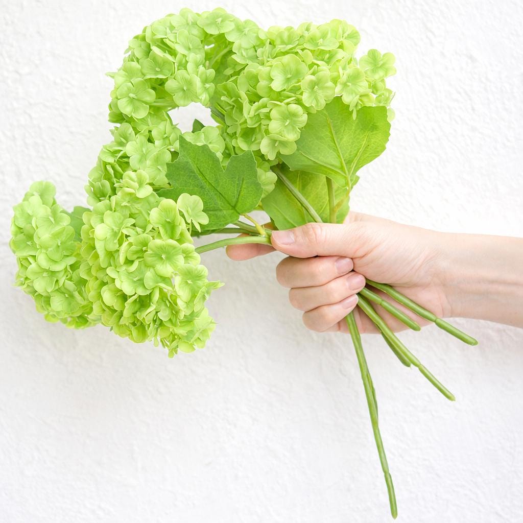 Hand holding six lime green real touch hydrangea stems to show bouquet size and scale.