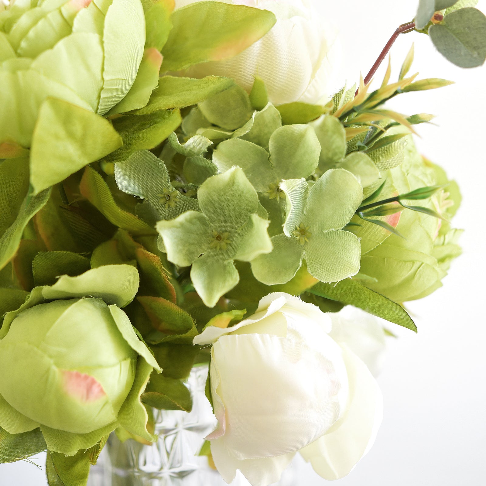 Close-up of moss green and cream artificial peony blooms, buds, hydrangea accents, and greenery.