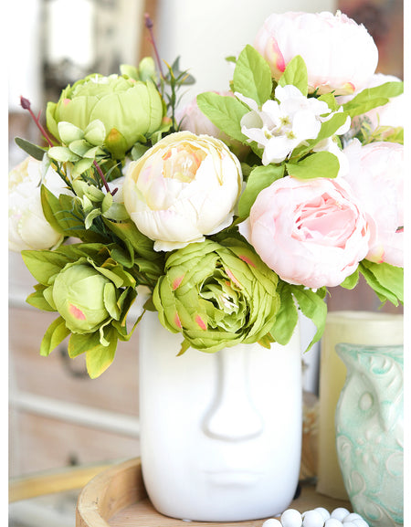 Moss green and cream faux peony bouquet bundles arranged in a white ceramic vase on a bright tabletop.