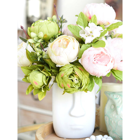 Moss green and cream faux peony bouquet bundles arranged in a white ceramic vase on a bright tabletop.