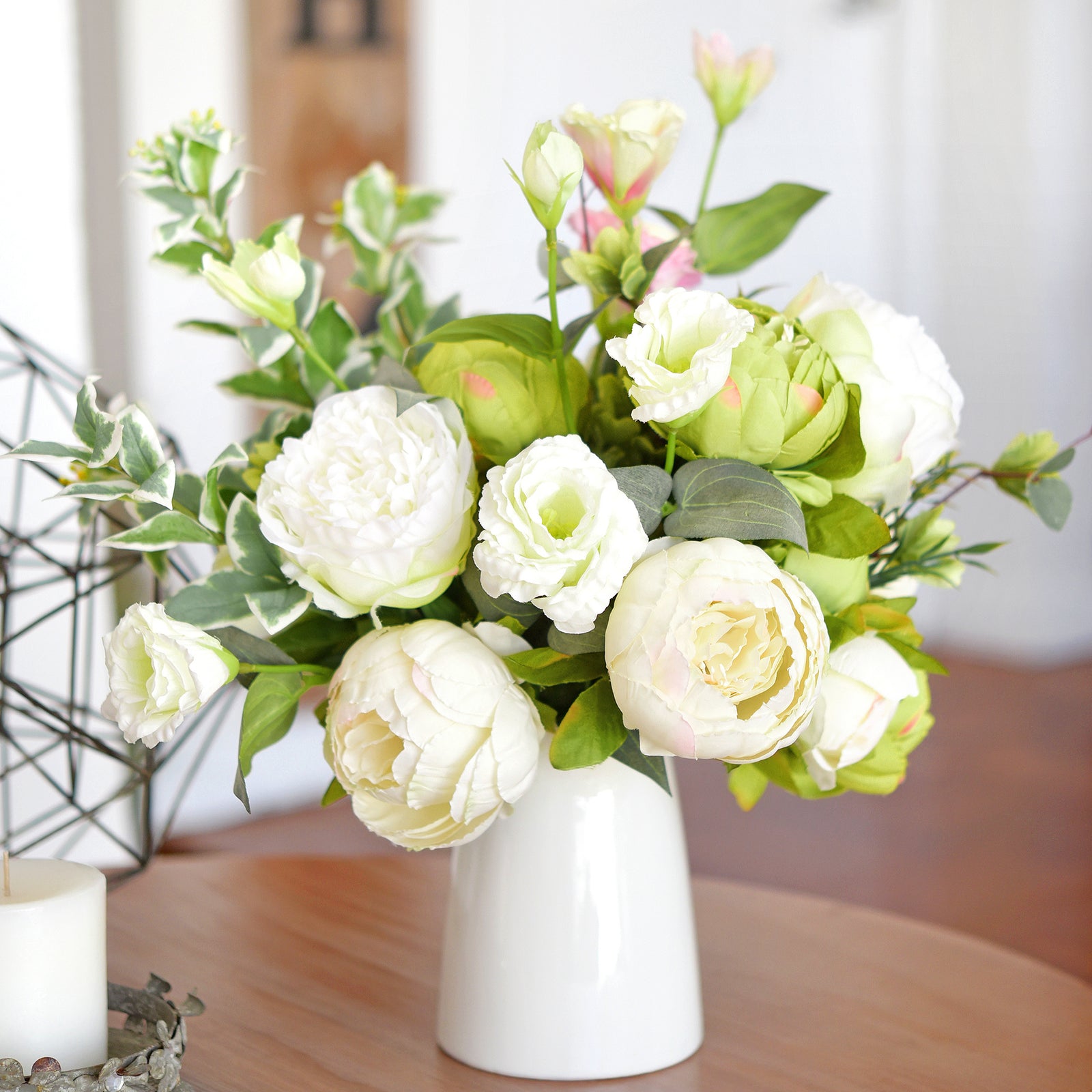 Moss green and cream faux peony bouquet styled in a white vase on a warm wooden table.