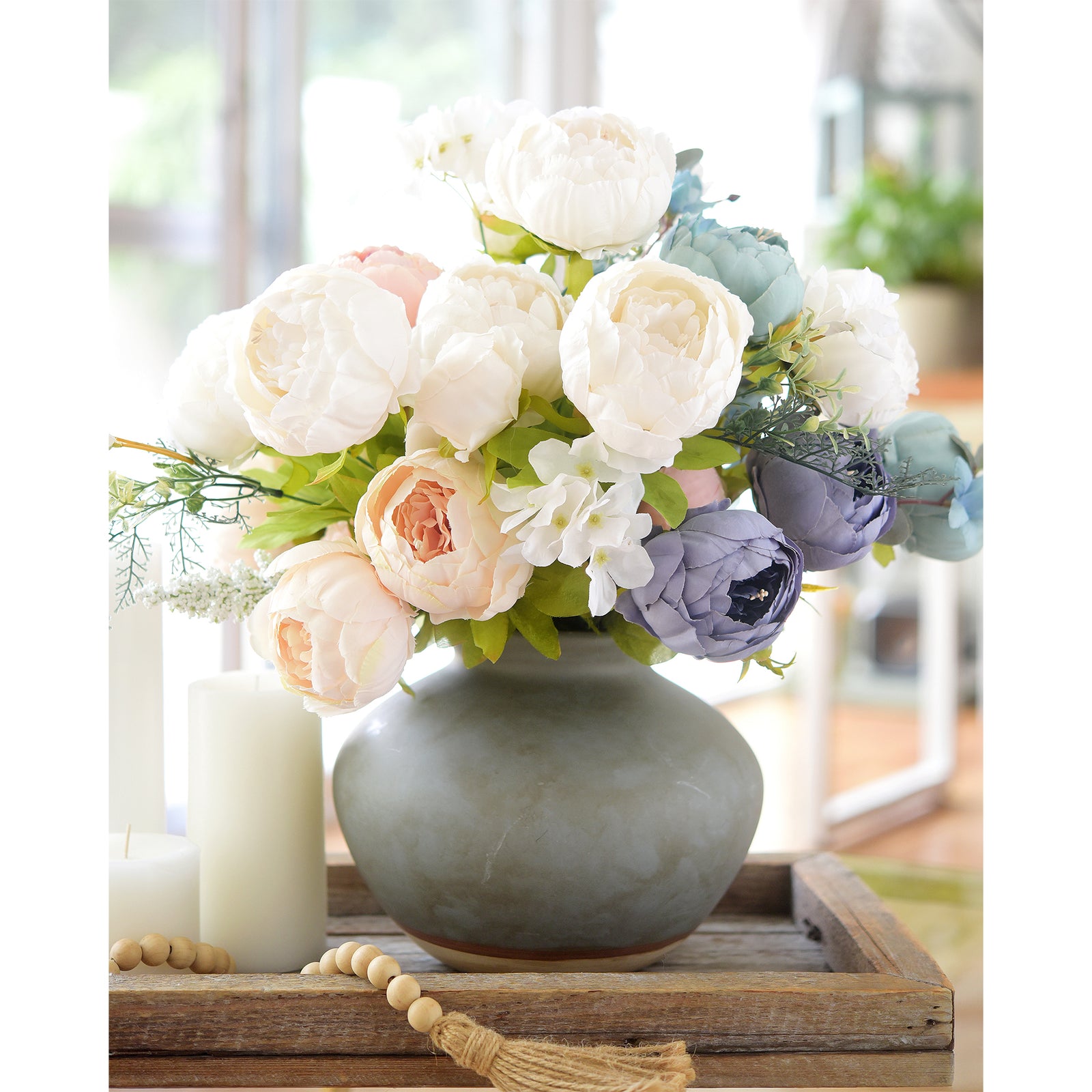 Pastel floral display with white and colored peonies, placed in a grey vase and styled alongside candles for cosy home accents.