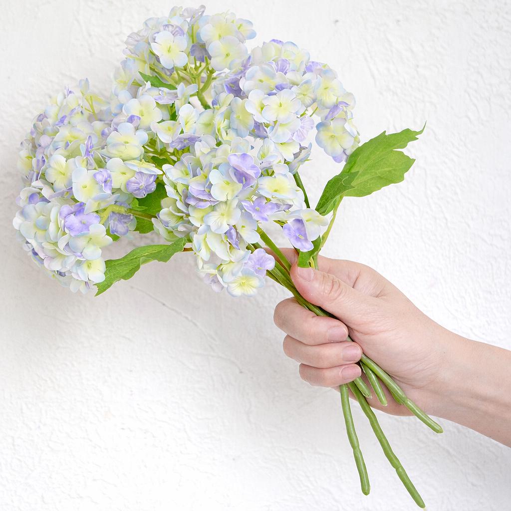 Hand holding six periwinkle and white real touch hydrangea stems to show bouquet size and scale.