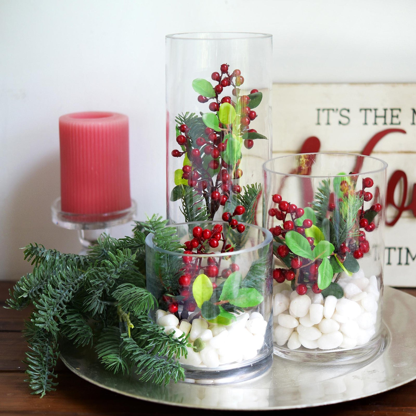 Bundle of soft-touch faux pine branches in round glass vases various heights juxtaposed together