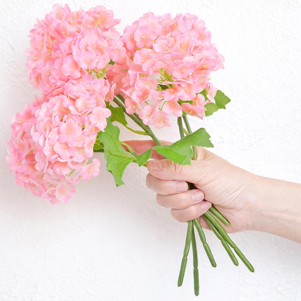 Hand holding six pink real touch hydrangea stems to show bouquet size and scale.