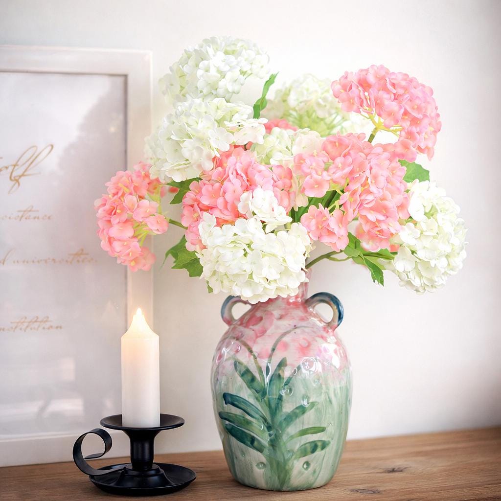 Pink and white hydrangea stems arranged in a decorative vase beside a candle.