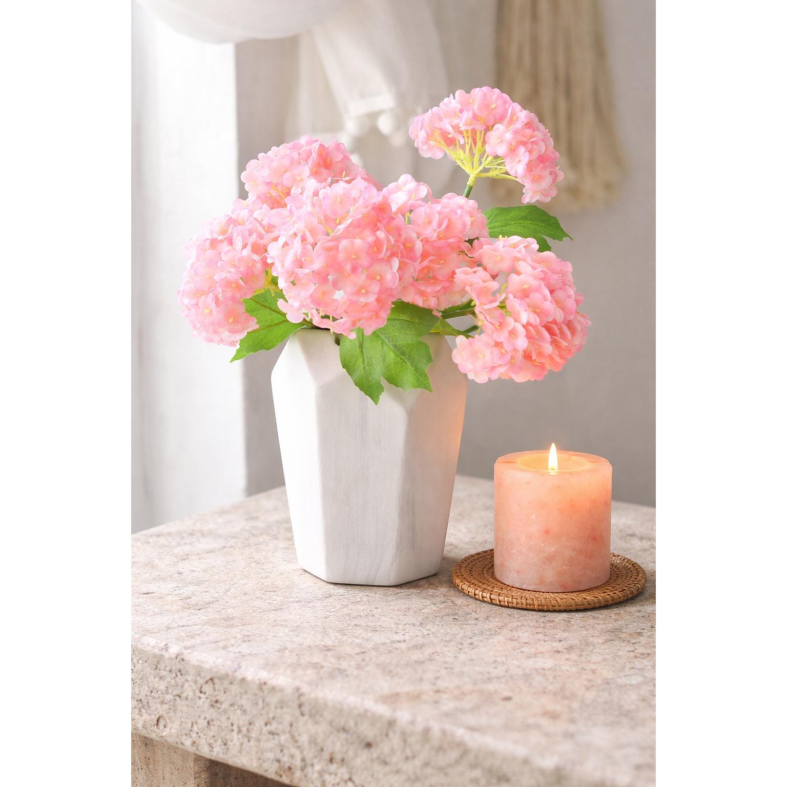 Pink real touch hydrangea stems displayed in a white vase beside a candle.