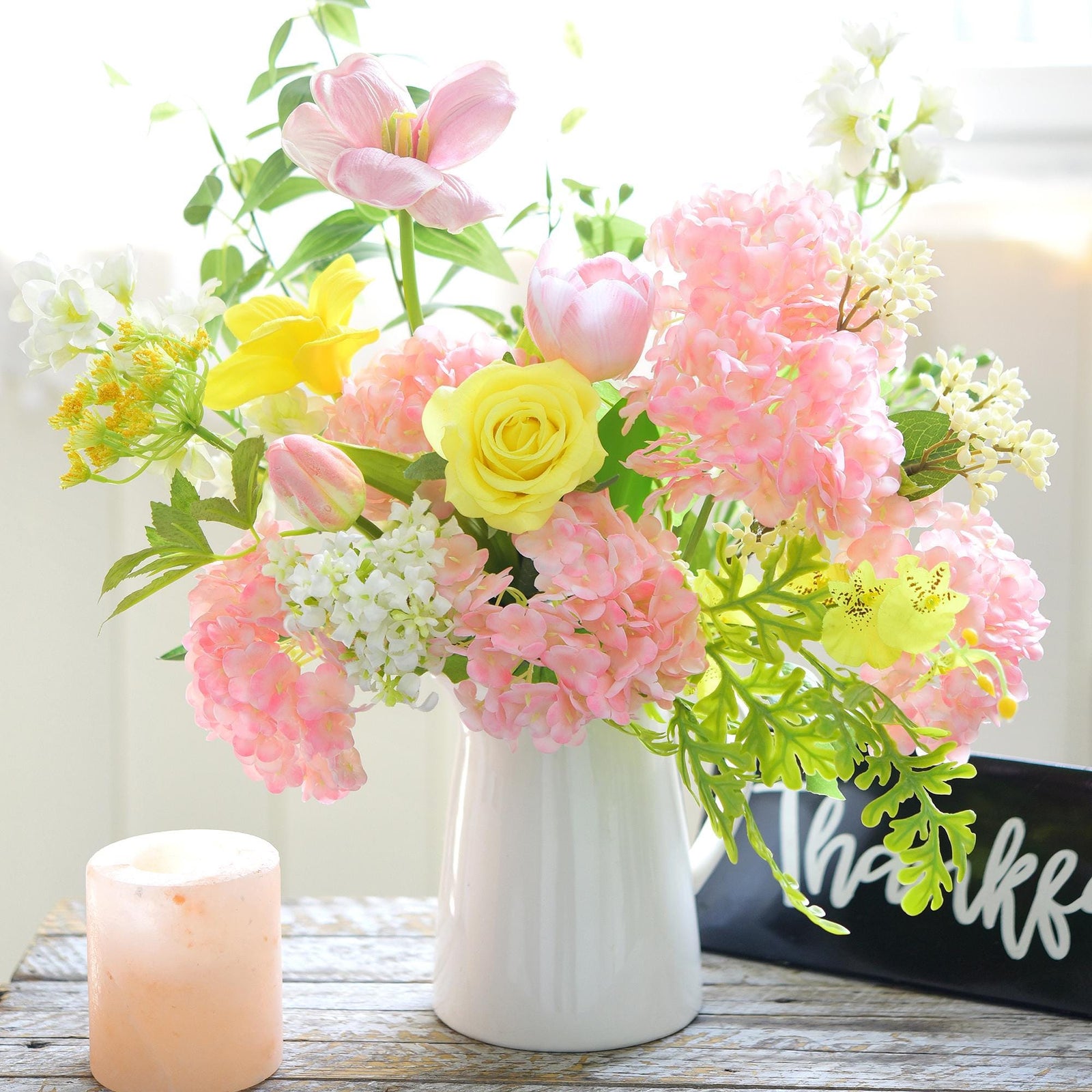 Pink hydrangea stems styled in a mixed floral centerpiece with yellow roses and greenery.
