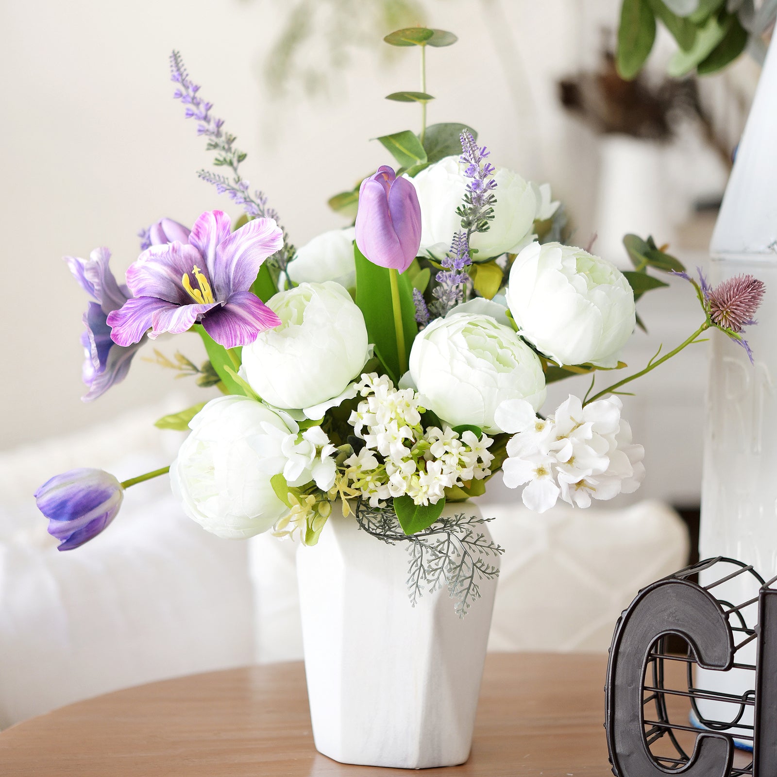 Purple and white floral arrangement featuring tulips, peonies, and greenery in a sleek white vase, perfect for spring décor.