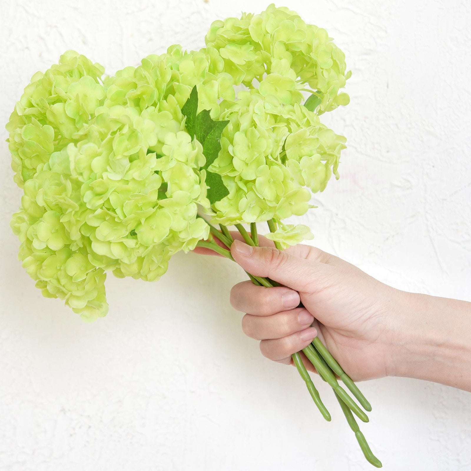 Hand holding six spring green real touch hydrangea stems to show bouquet size and scale.