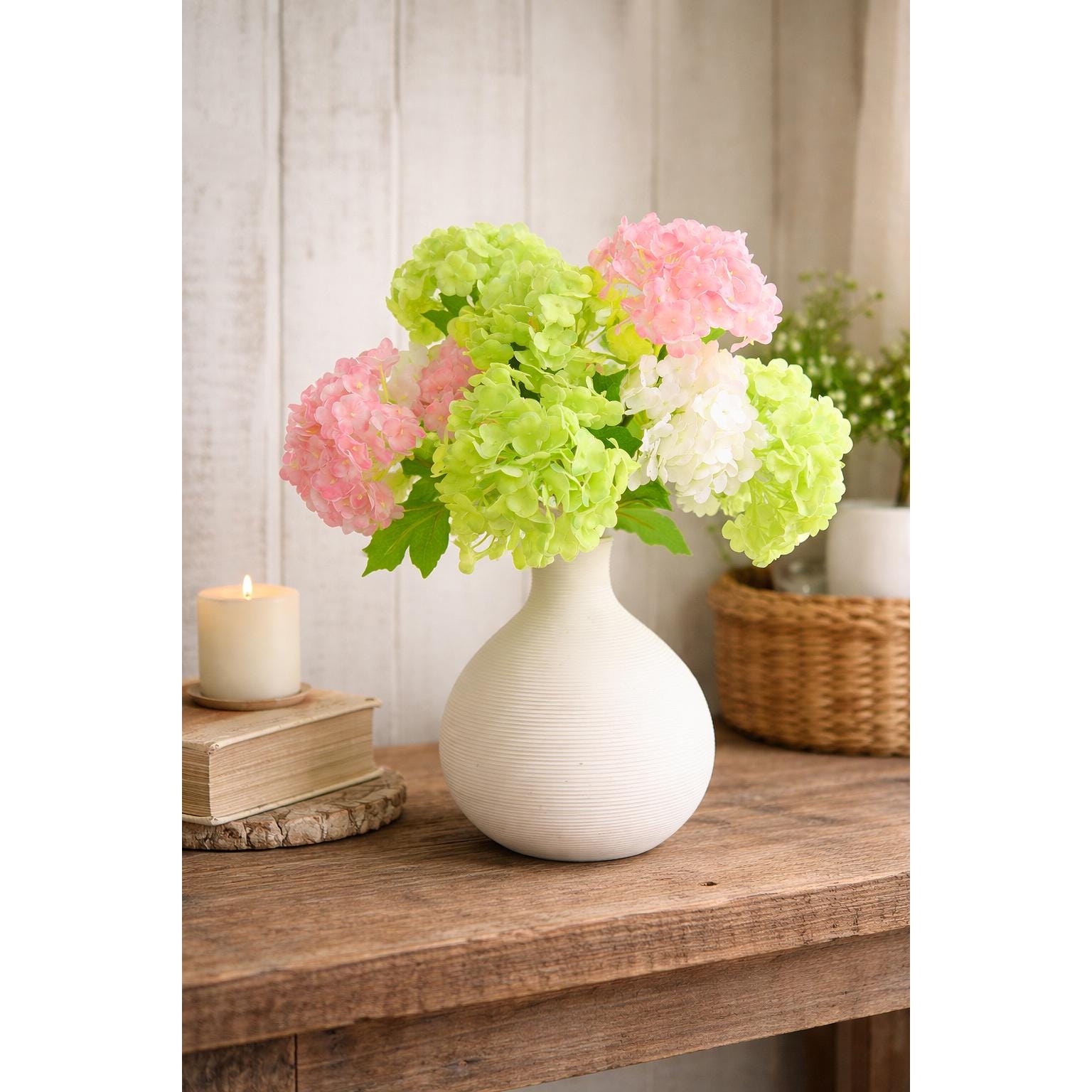 Spring green pink and white hydrangea stems arranged together in a white vase.
