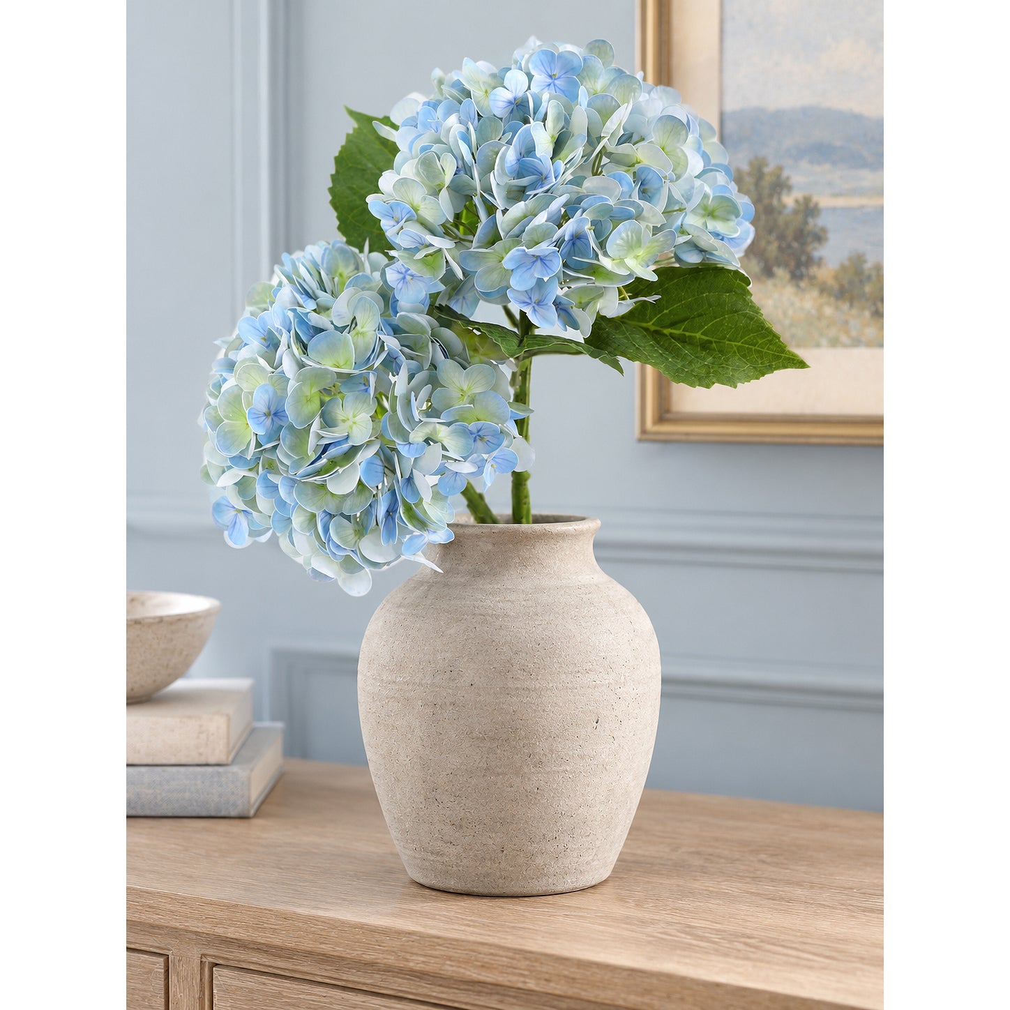 Two vintage blue green hydrangeas in a pale stoneware vase on a light wood console.