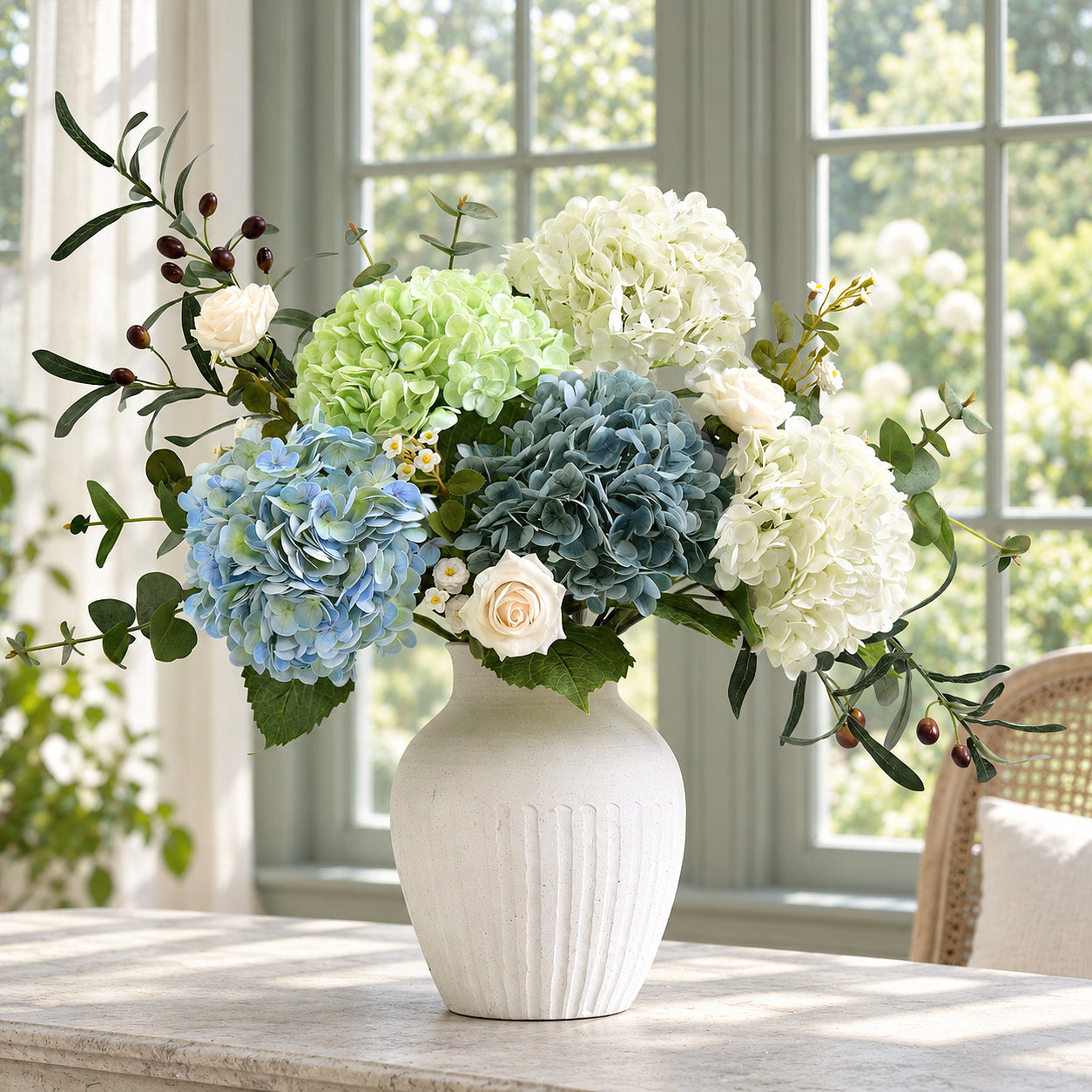 Vintage blue green hydrangeas with white, pale green and slate blue flowers in a white vase by a window.