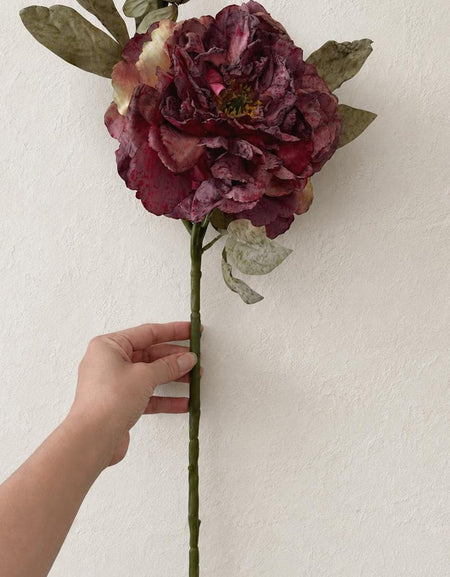 One dusty mauve artificial peony stem with an open bloom, buds and mottled green leaves on a white background.
