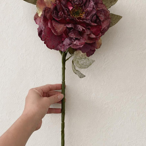One dusty mauve artificial peony stem with an open bloom, buds and mottled green leaves on a white background.