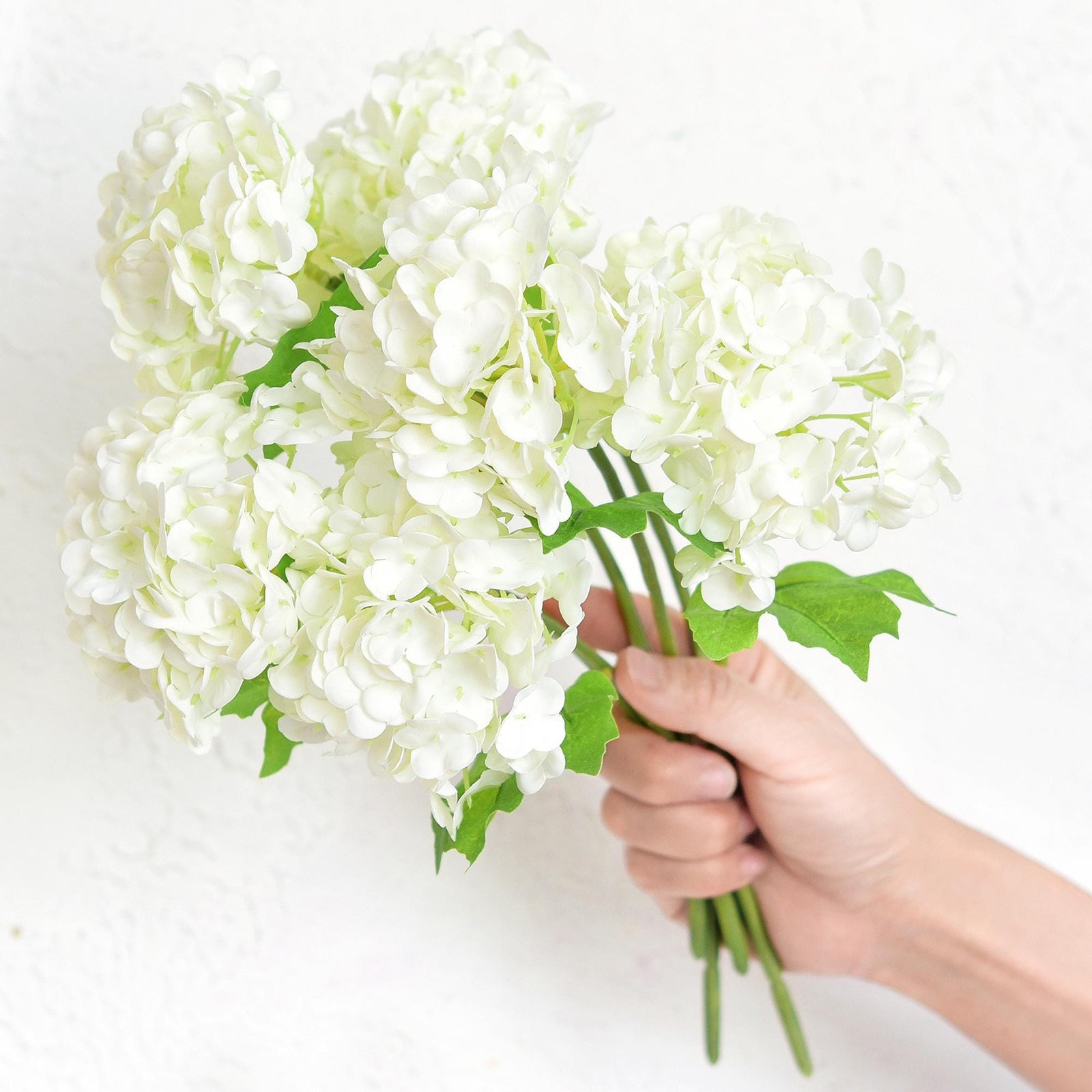 Hand holding six white real touch hydrangea stems to show bouquet size and scale.