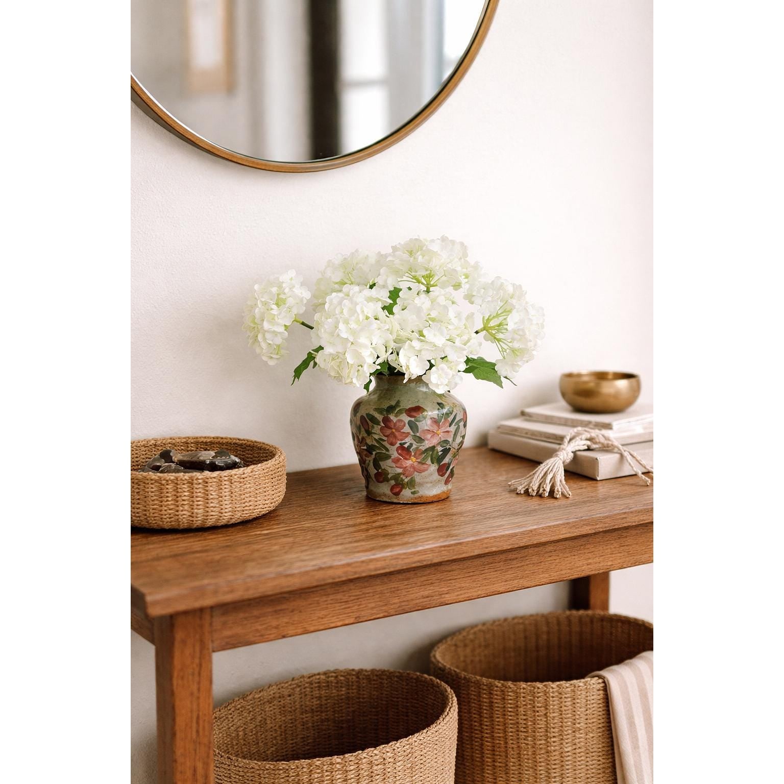 White hydrangea stems styled in a patterned vase on a wooden console table.