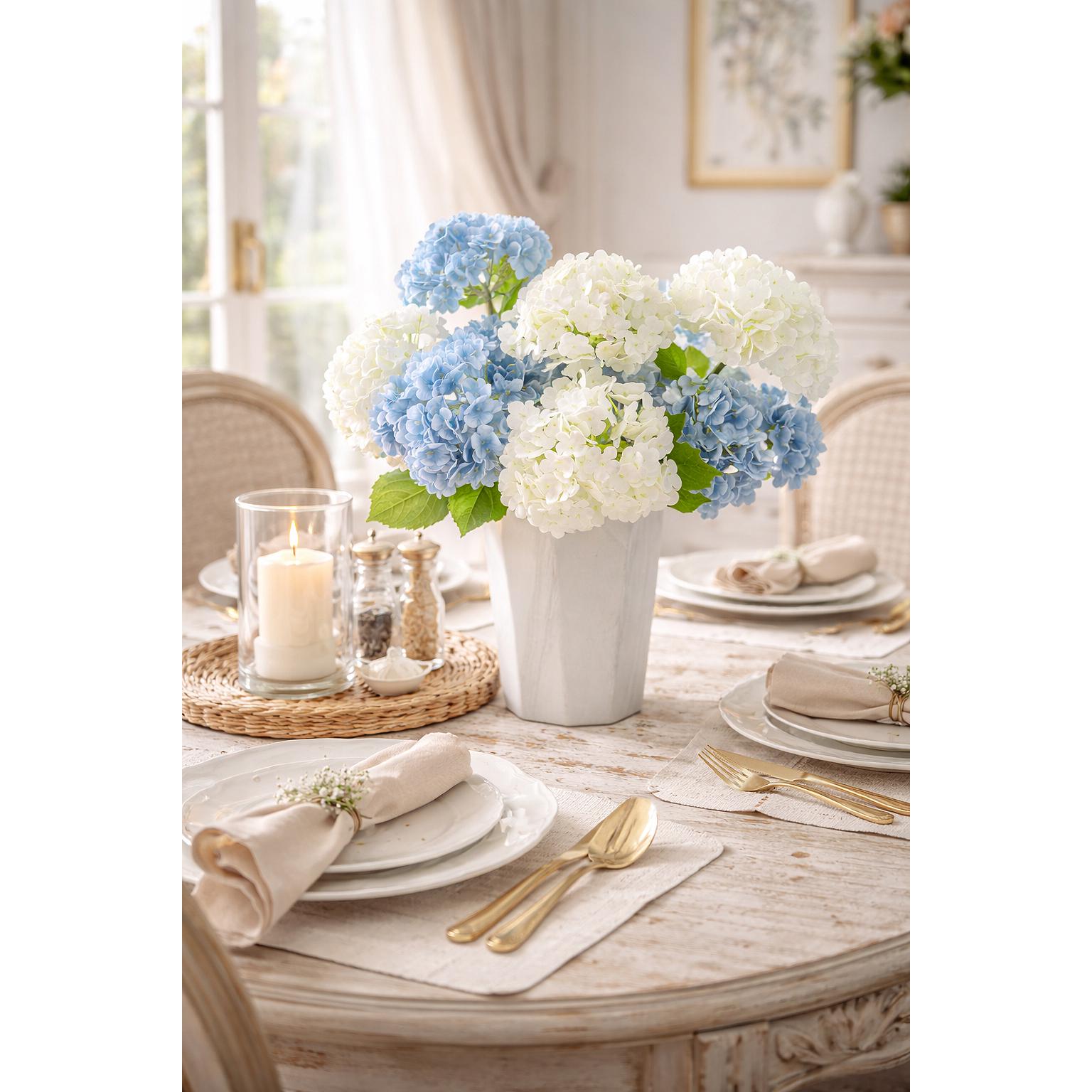 White and blue hydrangea stems arranged in a white vase on a styled dining table.