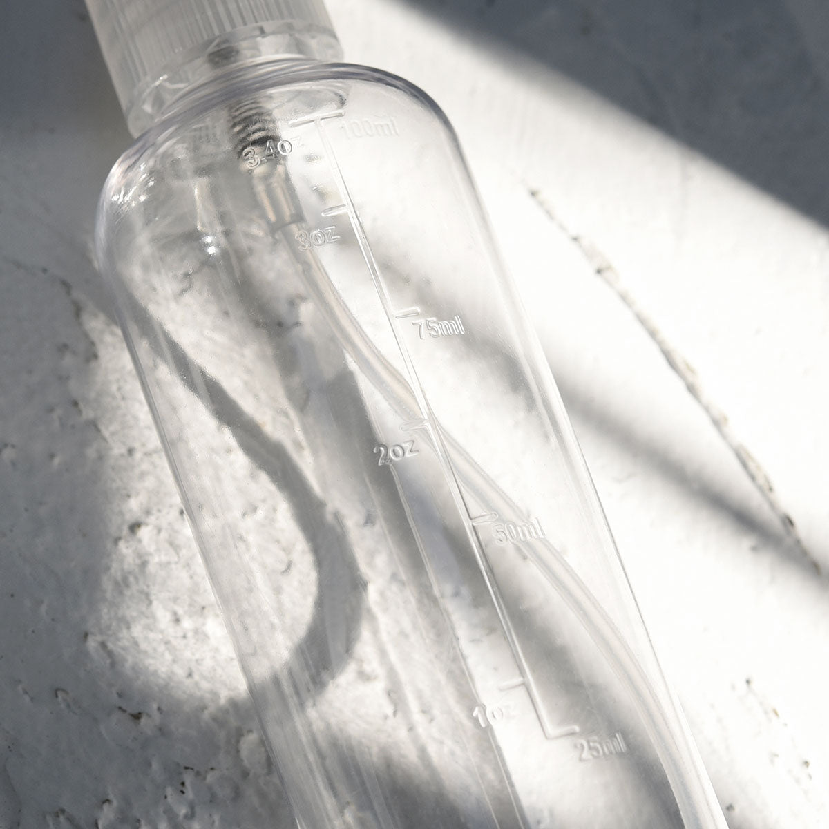 Close-up of clear 100ml travel bottle showing embossed volume markings in milliliters and ounces

