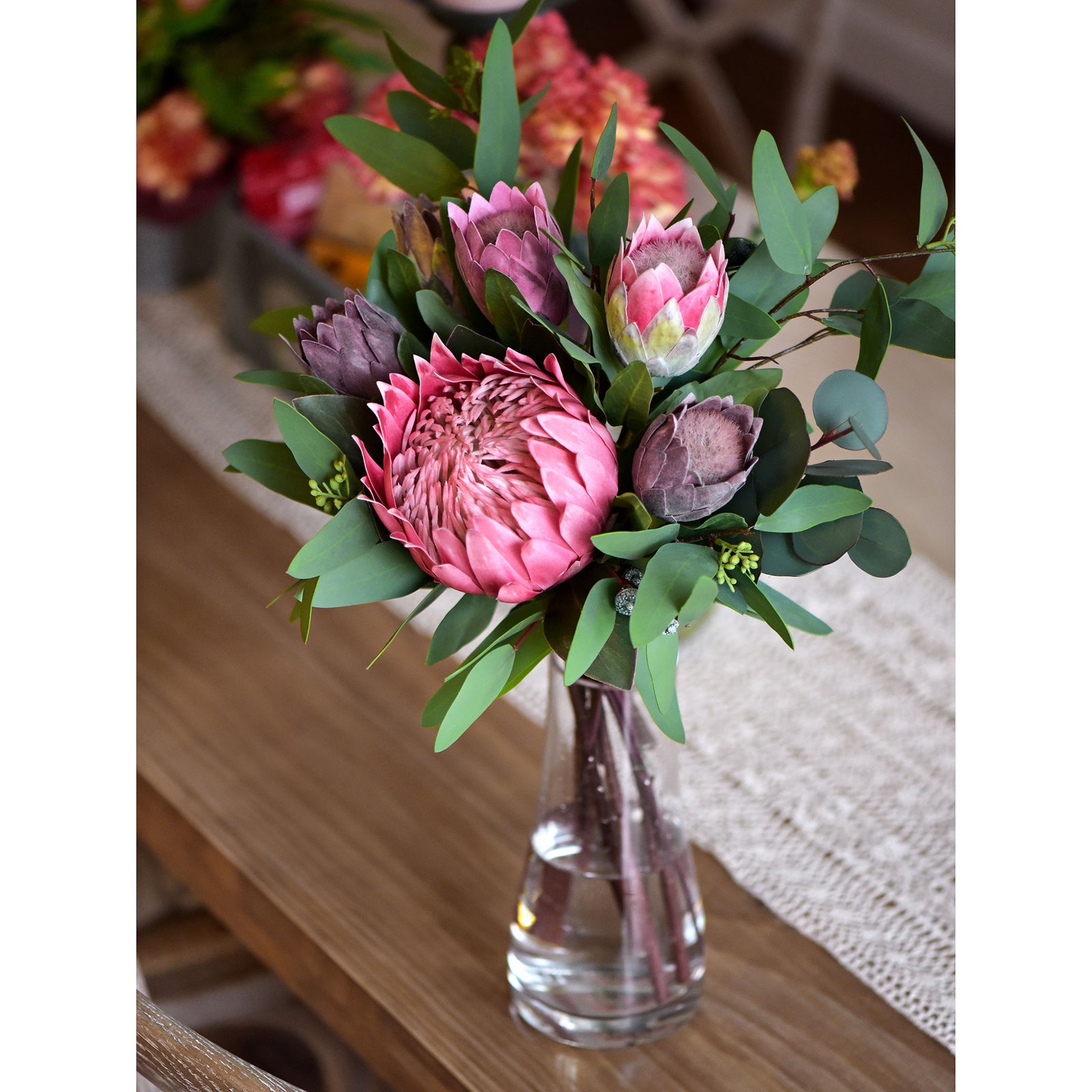 Dusty plum artificial baby protea stems showing compact blooms and green stems.